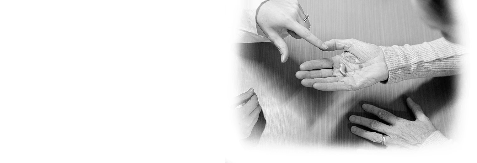 A woman points out a feature on a hearing aid. 