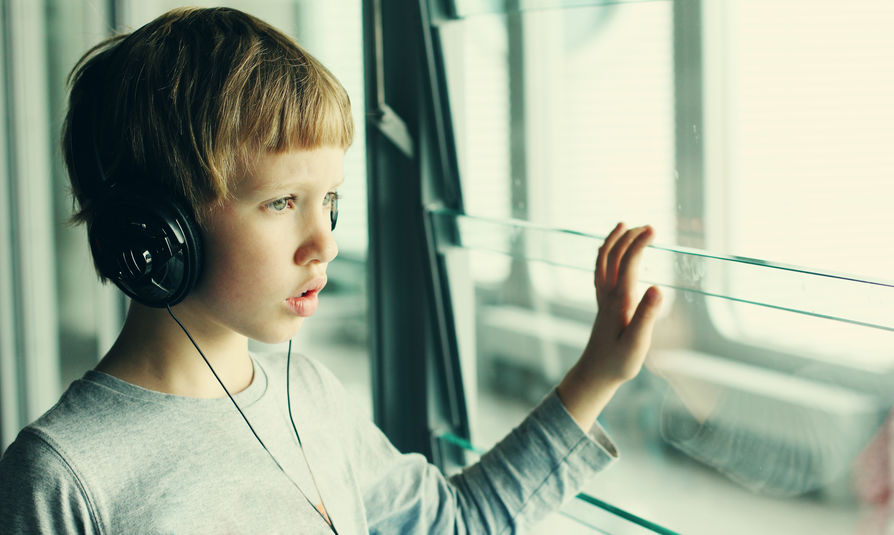 A boy with headphones on looks out the window. 