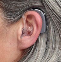 A picture of a woman wearing a behind-the-ear hearing aid with clear plastic earmold. 