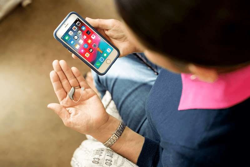 A woman looks at her smartphone and hearing aids. 