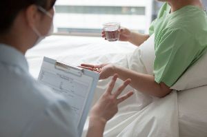 A hospital worker talks to a patient in a hospital bed.