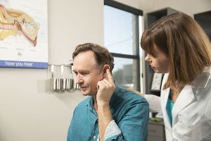 A man touches his hearing aid during an appointment.