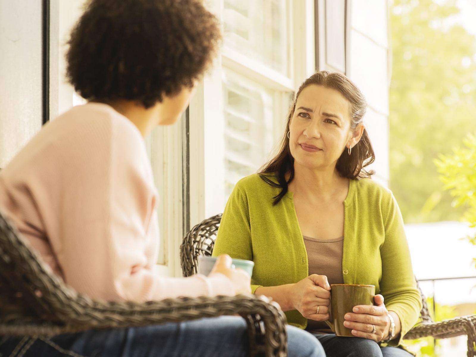 A woman with a hearing listens and watches a friend as she talks. 