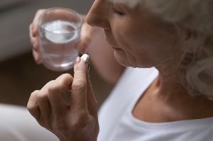 A woman taking a white tablet.